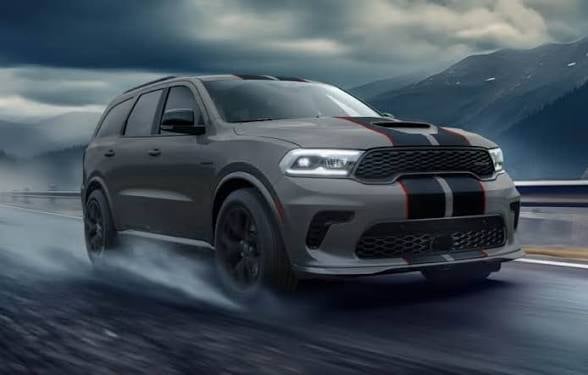 Grey Dodge Durango SUV with black racing stripes driving on wet mountain road in stormy weather