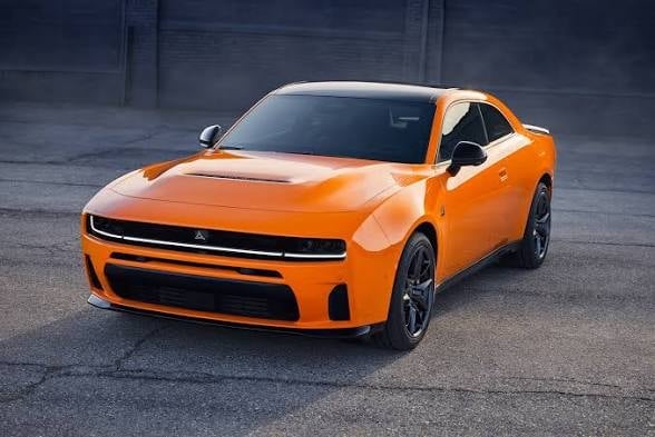 Bright orange Dodge Charger muscle car photographed from front three-quarter angle on a concrete surface