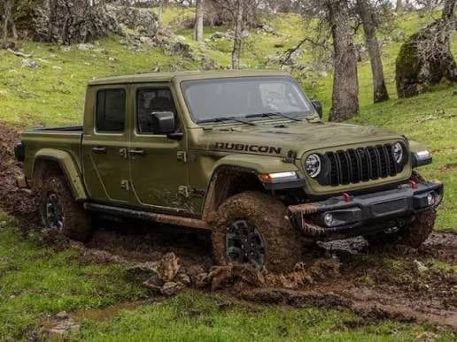 Olive green Jeep Gladiator Rubicon pickup truck parked on muddy grass with trees in background