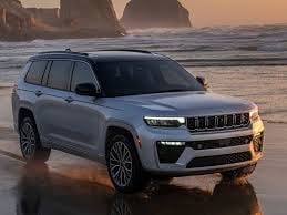 Blue Jeep Grand Cherokee SUV parked on beach at sunset with rocky cliffs in background