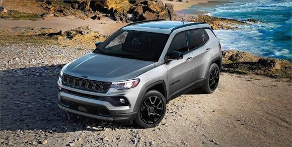 Silver Jeep SUV parked on rocky beach with turquoise ocean water in background