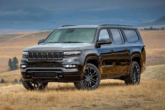 Black and blue Jeep Grand Wagoneer SUV parked in a dry, hilly landscape under a cloudy sky